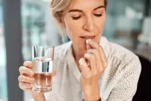 Femme agée prenant la vitamine avec un verre de l'eau dans sa main