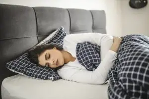 Jeune femme allongée dans son lit et souffrant de fatigue et stress, mais aussi de crampes menstruelles à la maison